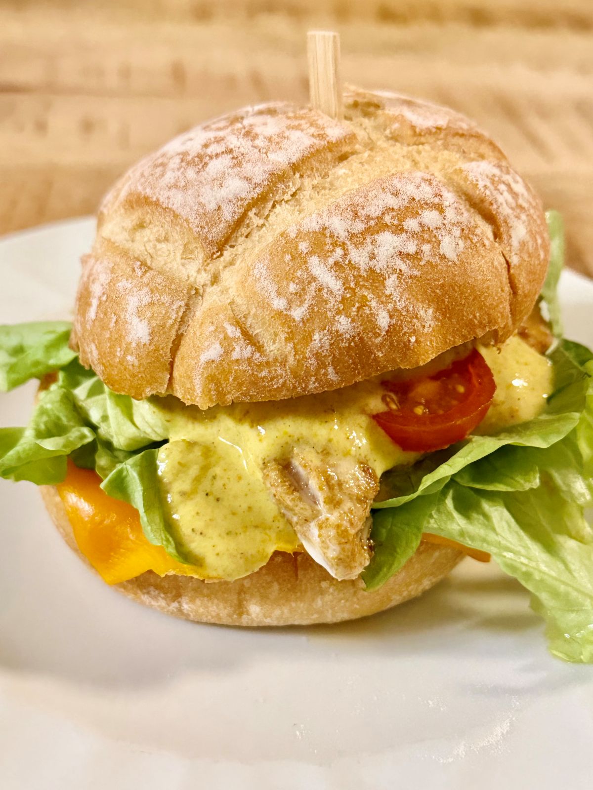 Hamburger au poulet, sauce yaourt et curry, mimolette, tomate et salade
