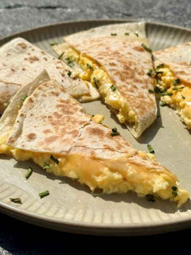 Quesadillas aux œufs brouillés et aux 3 fromages coupées en deux, fromage fondant qui file