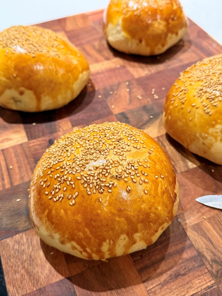 Buns burgers dorés au sésame sur la planche en bois, à la sortie du four