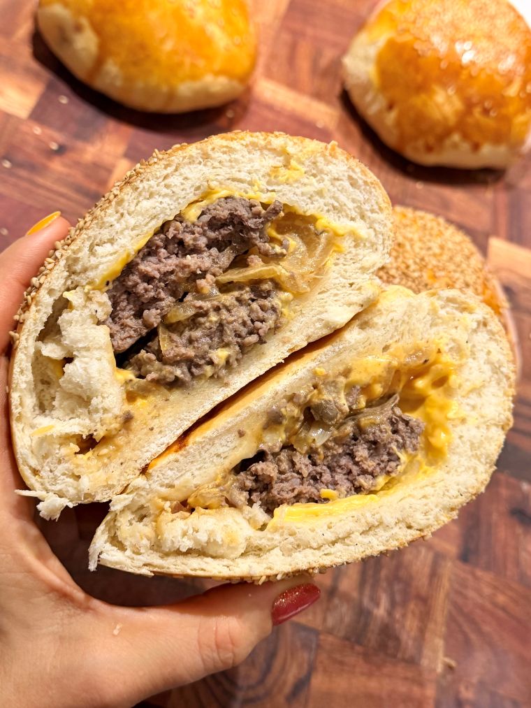 Bun burger maison coupé en deux et tenu à la main, les deux moitiés montrant le double steak et le cheddar fondu