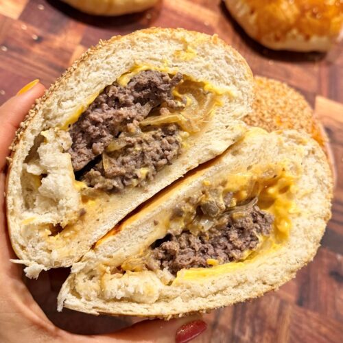 Bun burger maison coupé en deux et tenu à la main, les deux moitiés montrant le double steak, les oignons, la sauce burger et le cheddar fondu, un pain moelleux autour