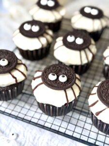 Cupcakes Halloween sur une grille, avec une base cacao, un glaçage crem cheese, un demi-Oreo sur le dessus, des pattes au chocolat et des yeux comestibles
