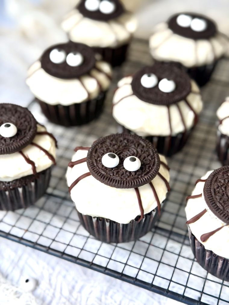 Cupcakes Halloween sur une grille, avec une base cacao, un glaçage crem cheese, un demi-Oreo sur le dessus, des pattes au chocolat et des yeux comestibles