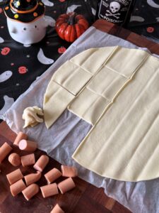 Couper la pâte feuilletés en carrés pour ensuite draper chaque morceau de saucisse